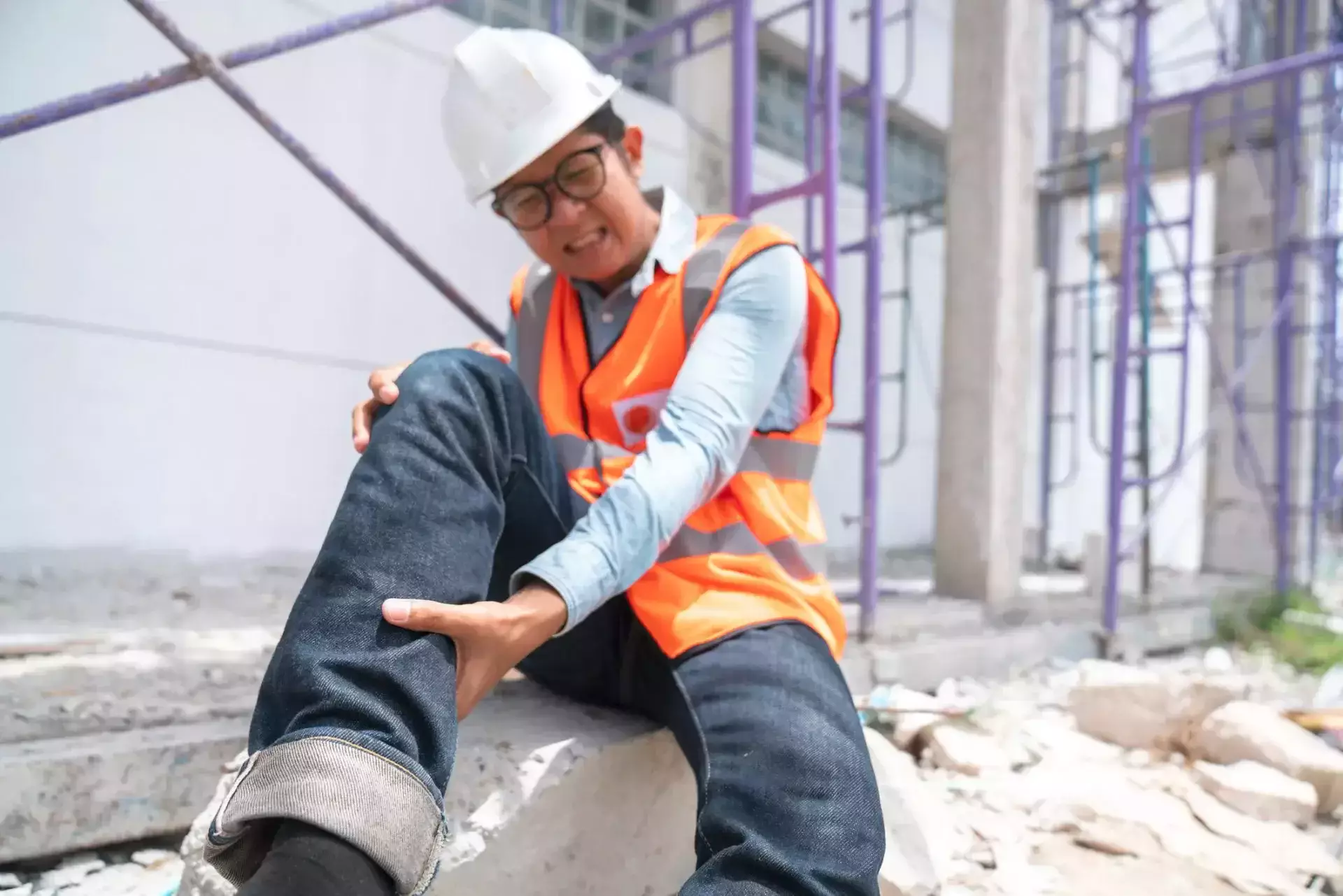 Trabajador de la construcción herido agarrándose la pierna de dolor en un sitio de construcción.