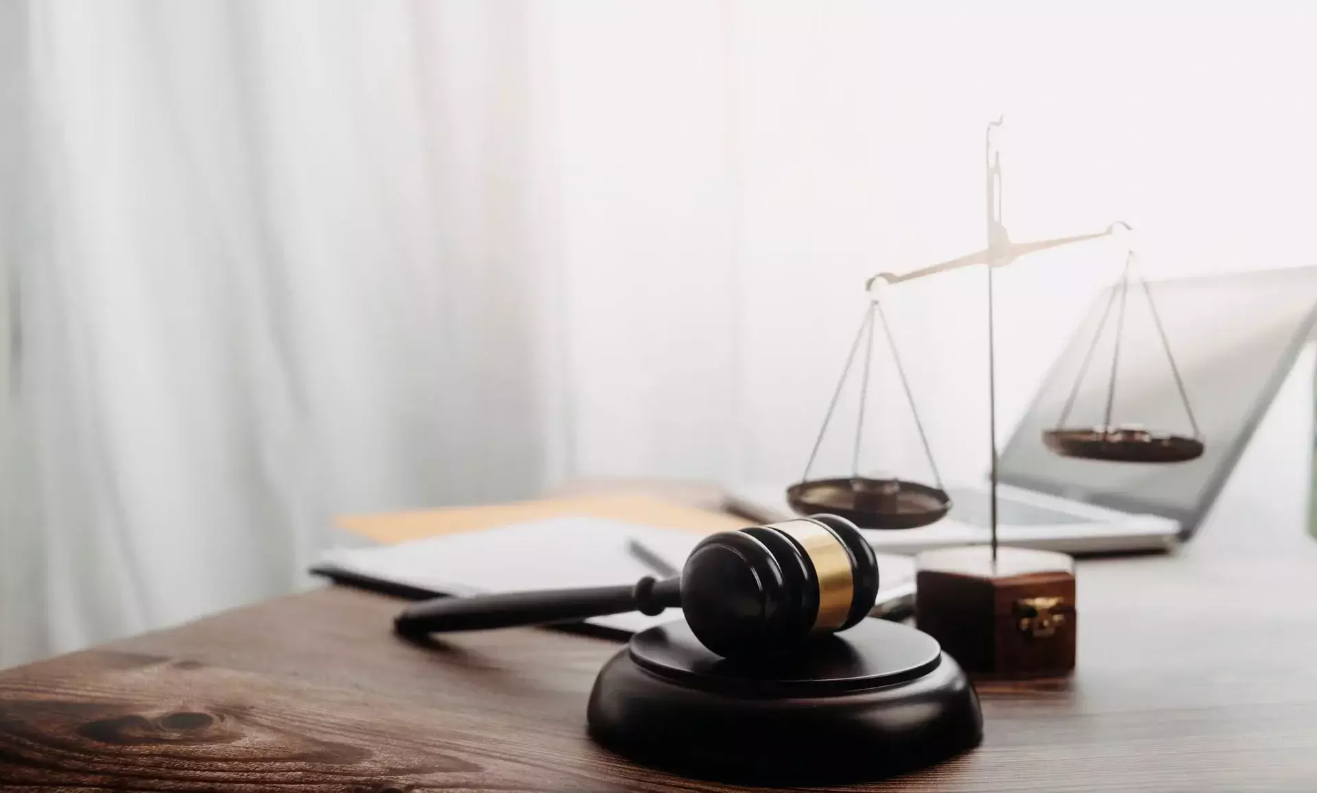 Judge's gavel, scales of justice, and open laptop on a wooden desk in a legal office setting.