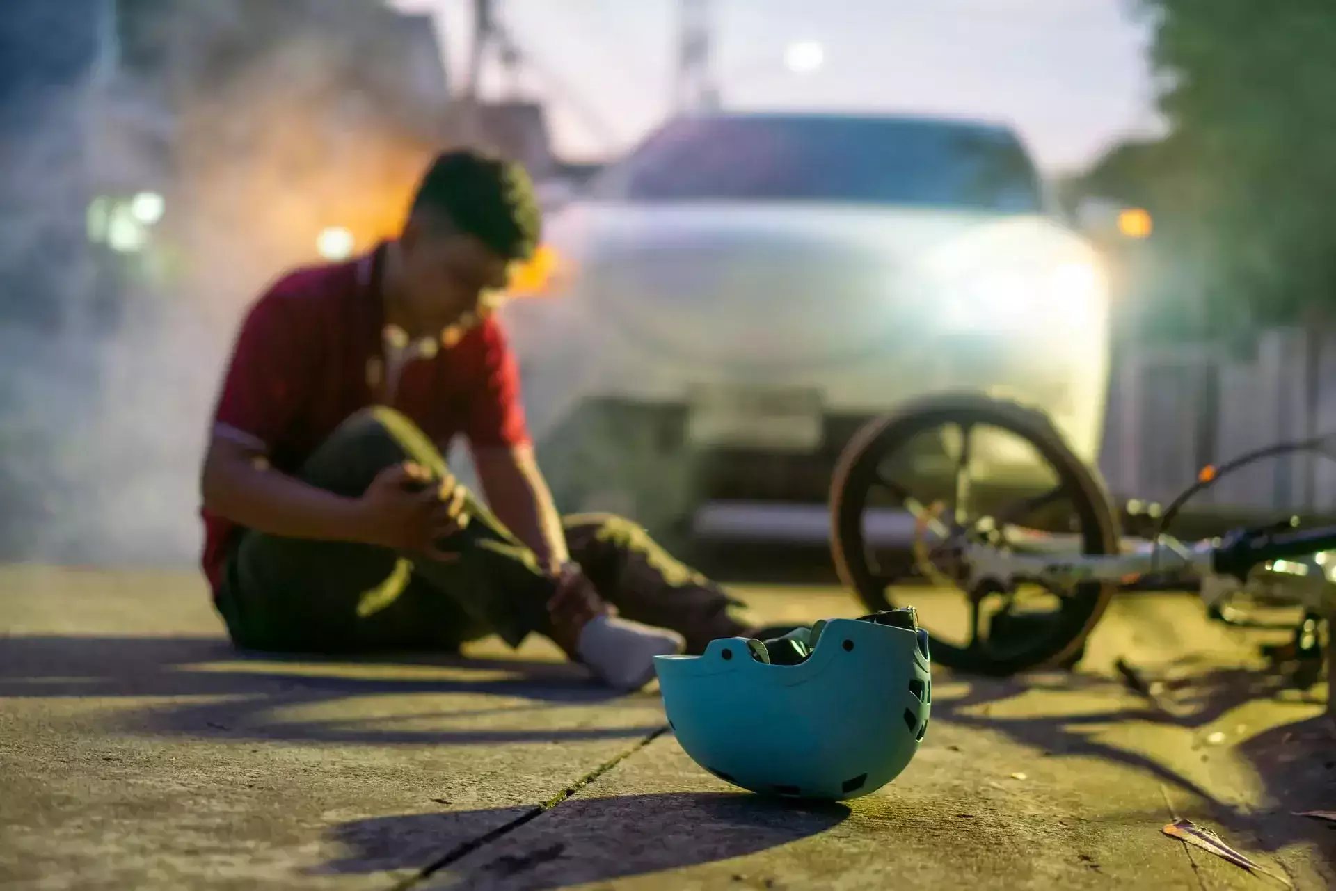 Injured cyclist sitting on the road after a bicycle accident with a helmet and bicycle nearby