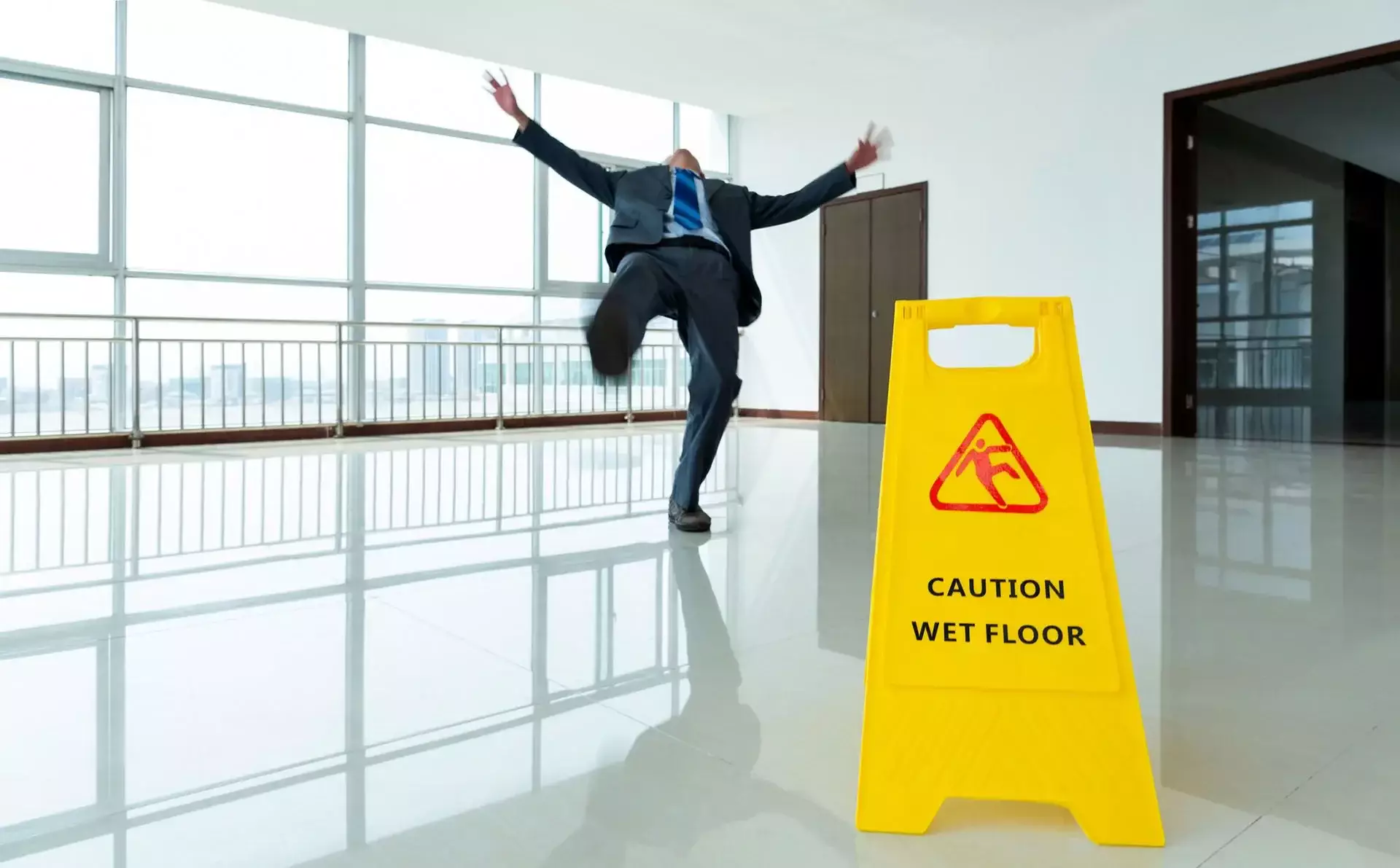 A man slipping on a wet floor beside a 'Caution Wet Floor' sign.