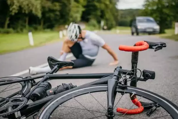 A fallen bicycle on the road with an injured cyclist behind.