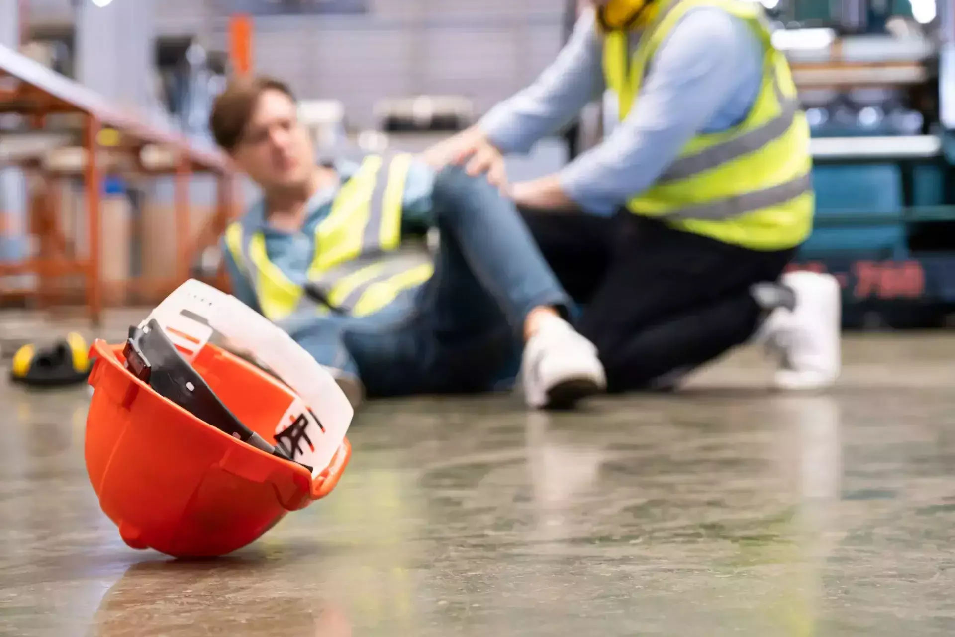 An orange hard hat on the floor with an injured worker behind.