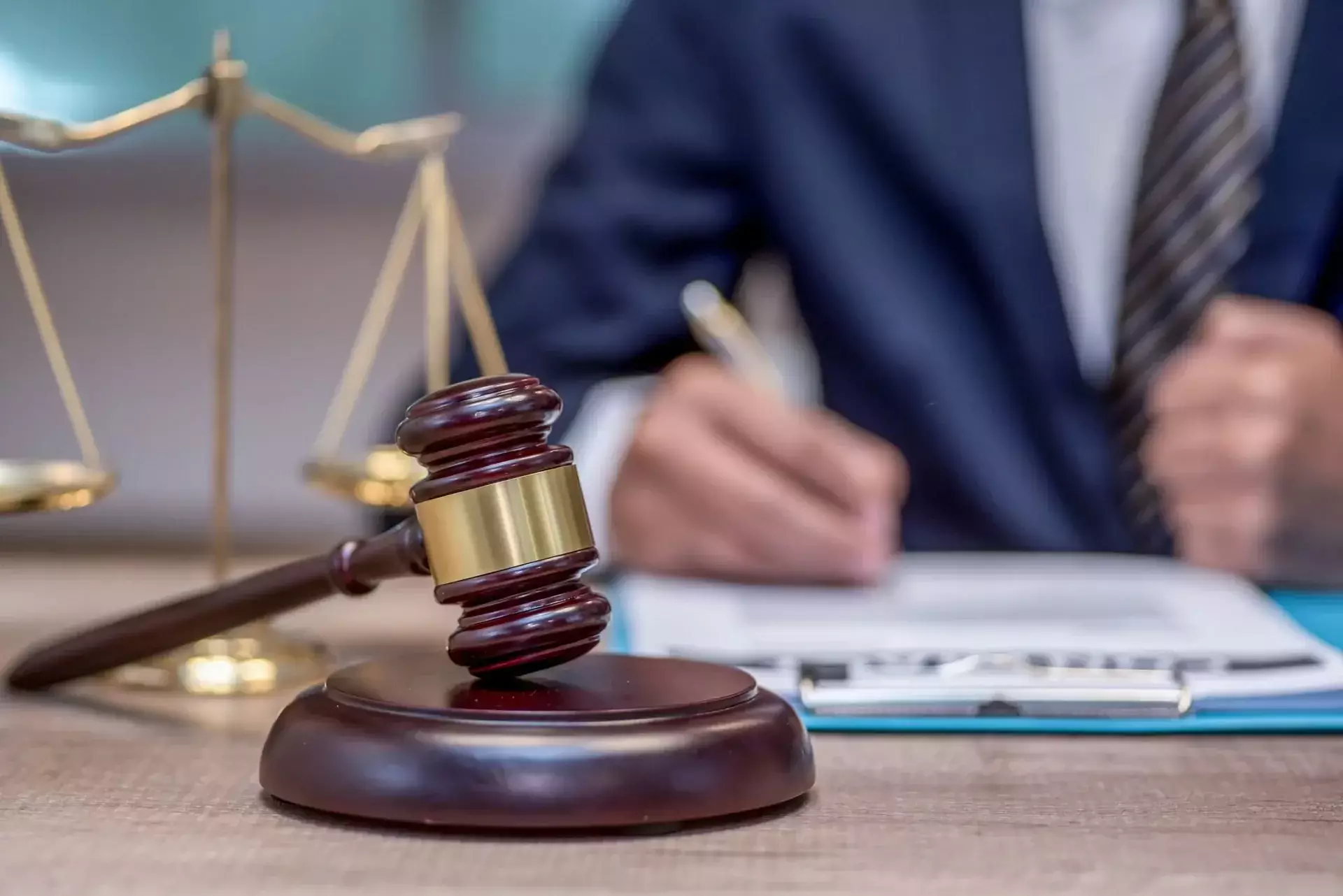 Judge’s gavel and scales of justice with a lawyer reviewing legal documents in the background
