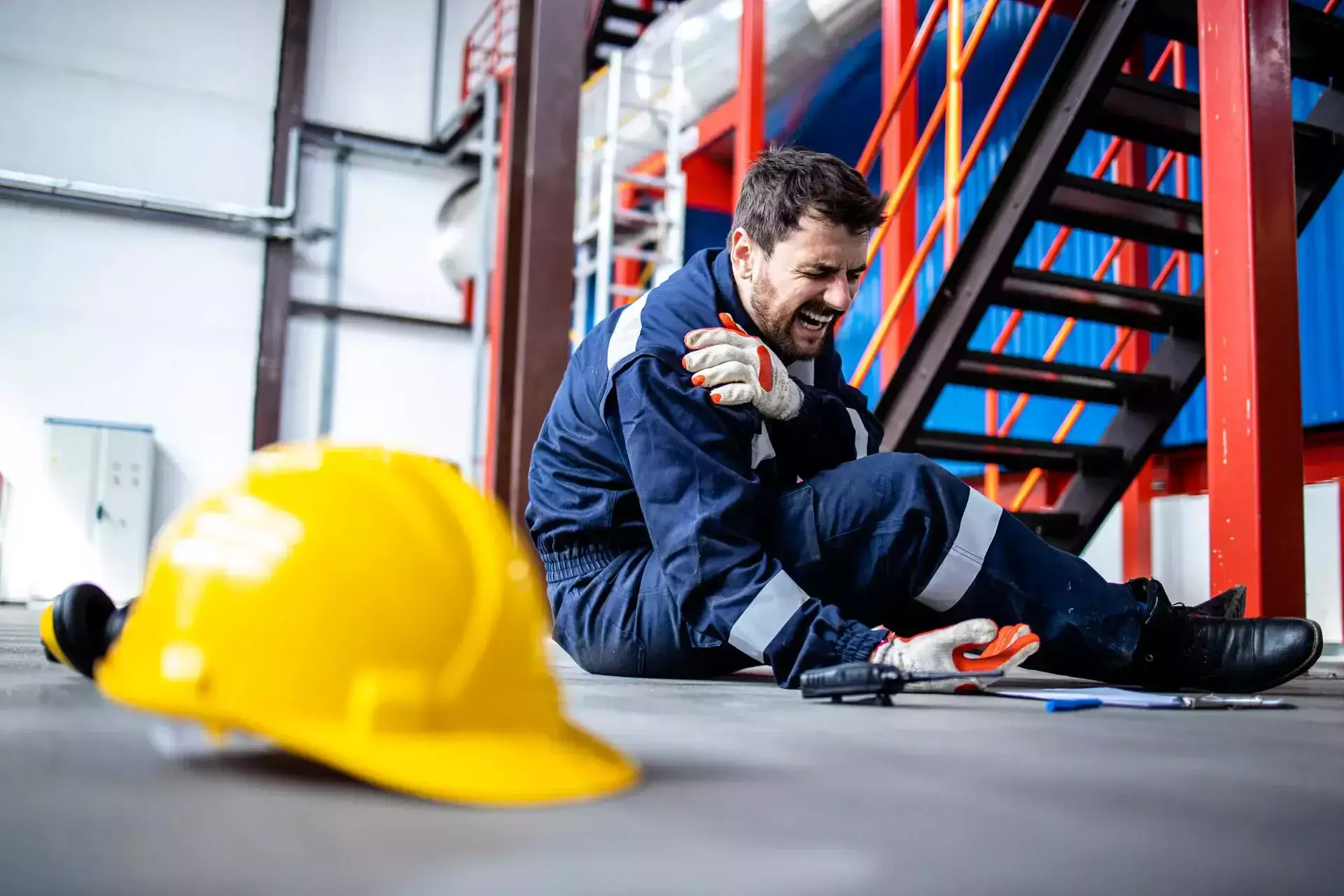 A worker sitting on the factory floor holding his injured shoulder.