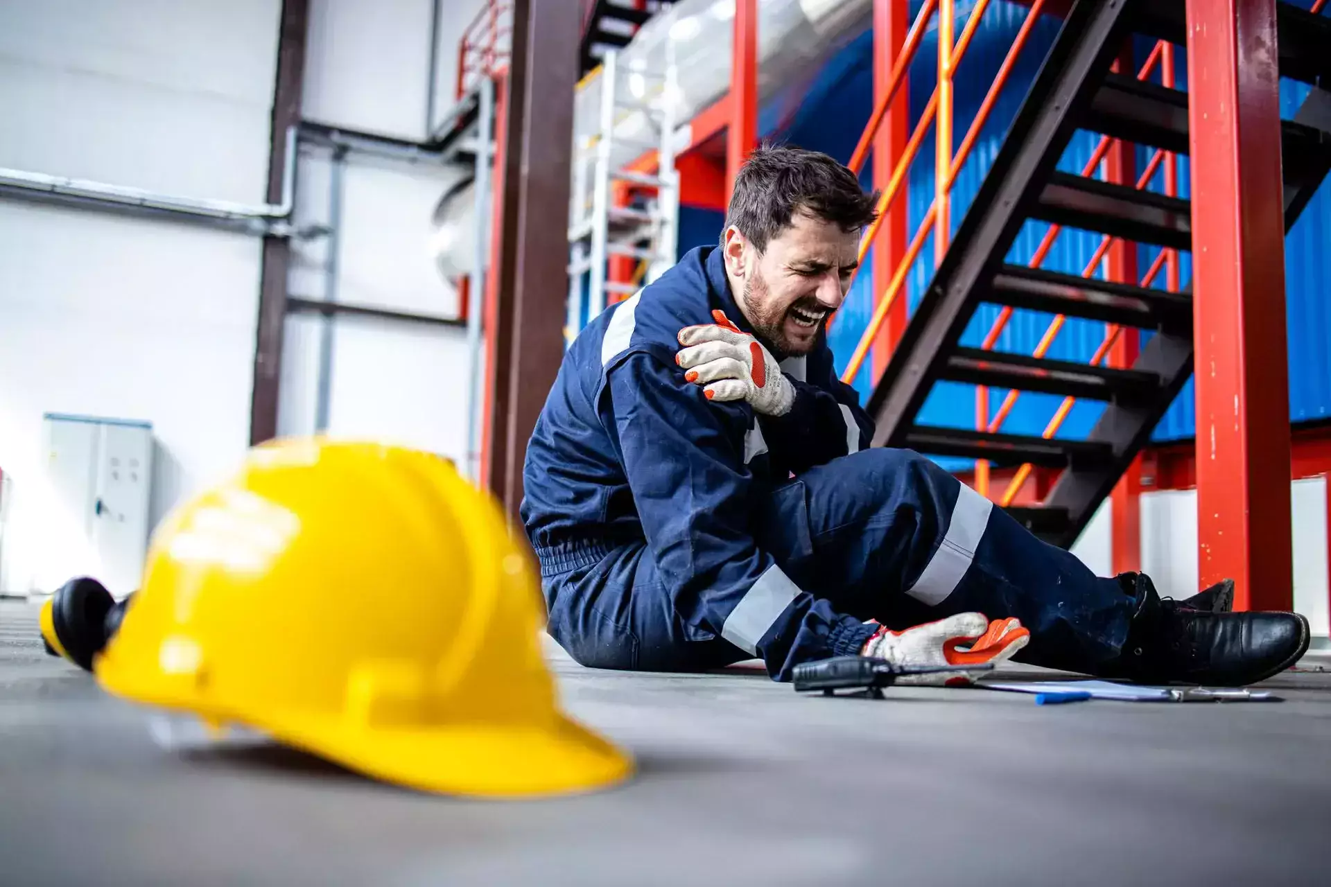 A worker sitting on the factory floor holding his injured shoulder.