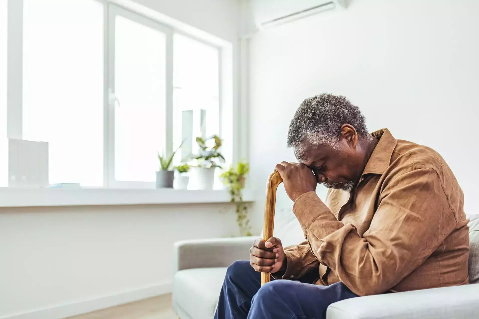 An elderly man sitting on a sofa and leaning on his cane.