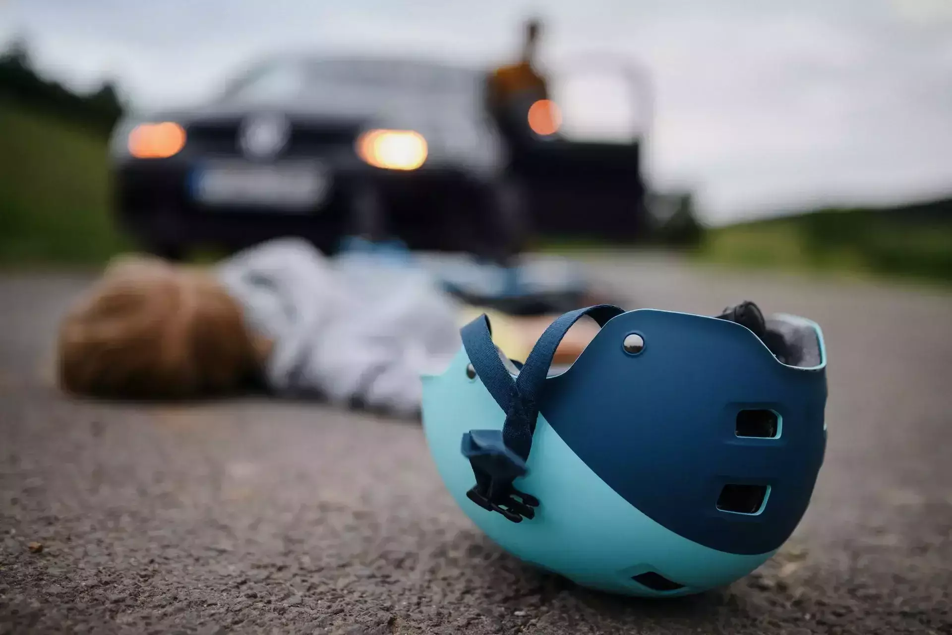 Cyclist lying injured on the road after an accident with a bicycle helmet and car nearby