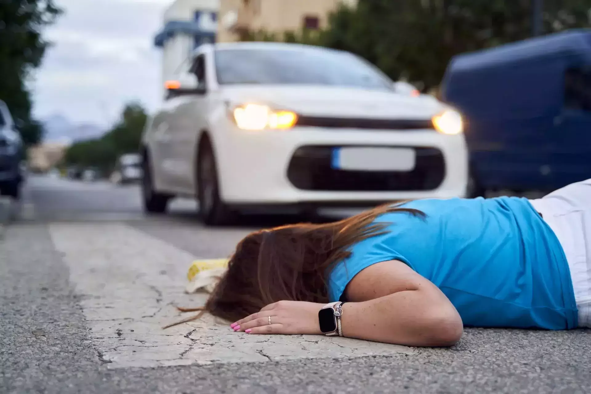 A person lying on the road in front of a white car after an accident.