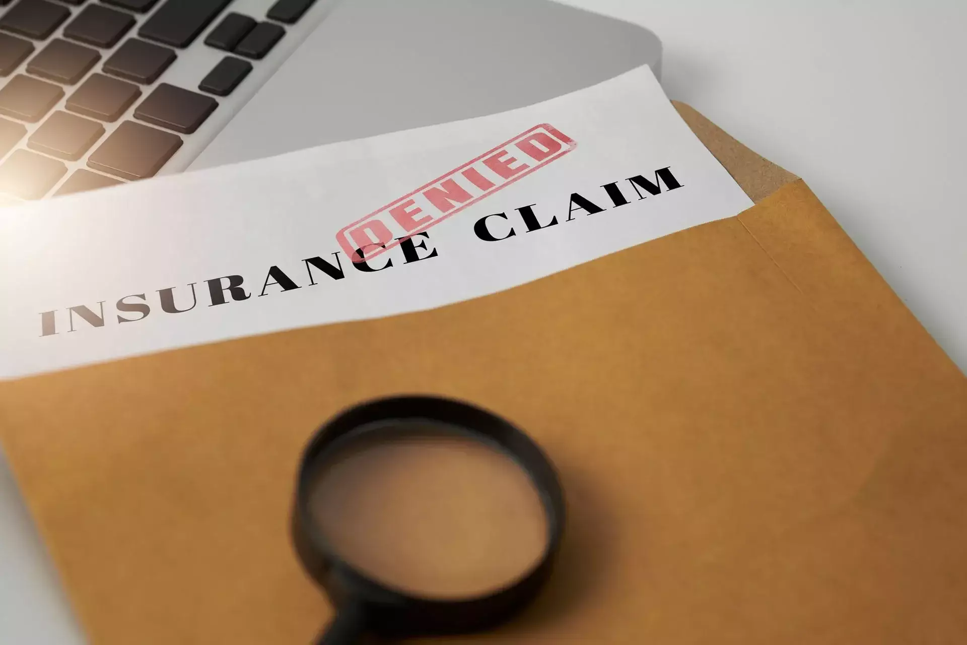'Insurance Claim' document with a red 'Denied' stamp on a brown envelope.