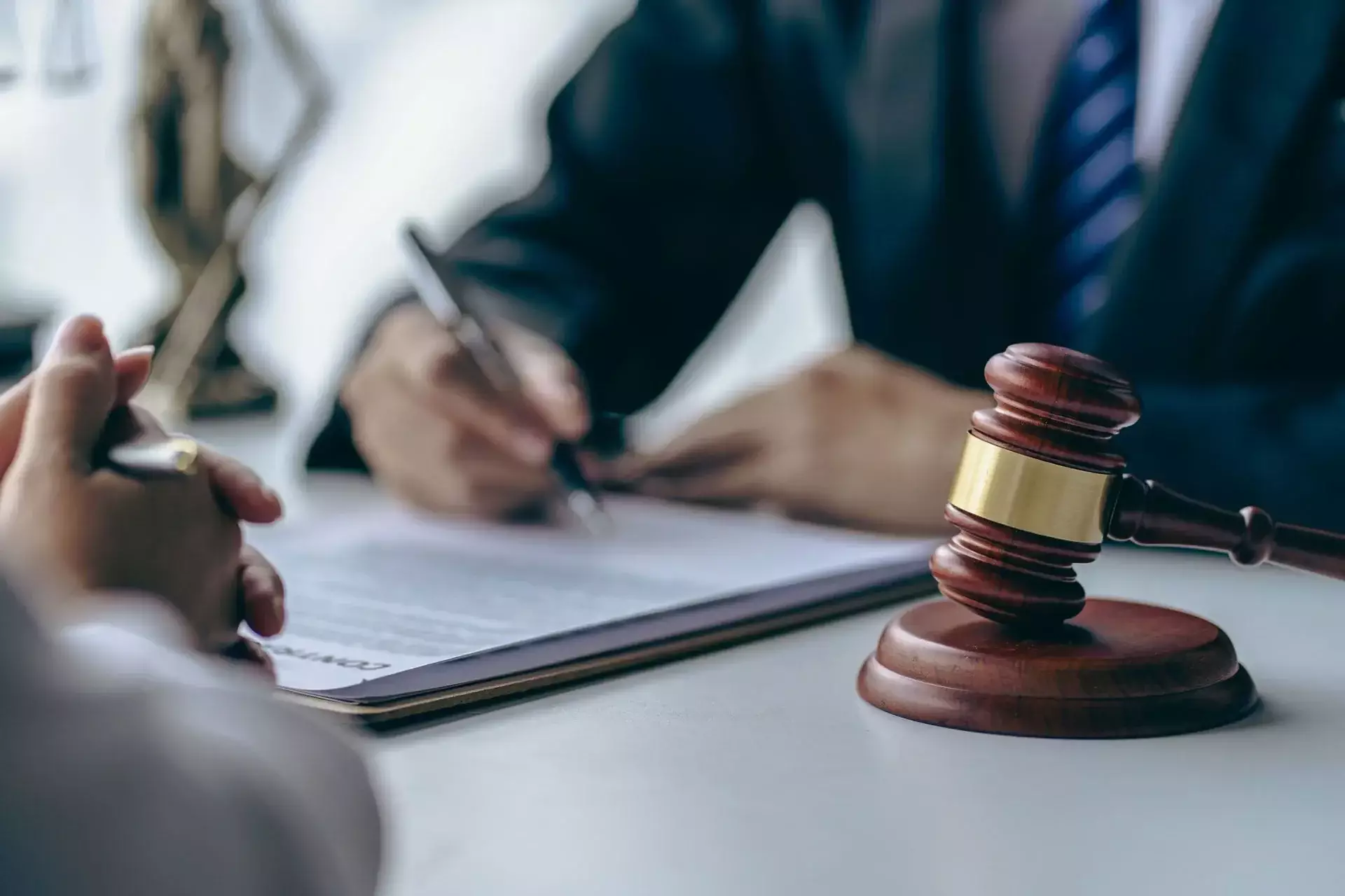 Wooden judge's gavel on desk with blurred person signing a document in formal legal setting.
