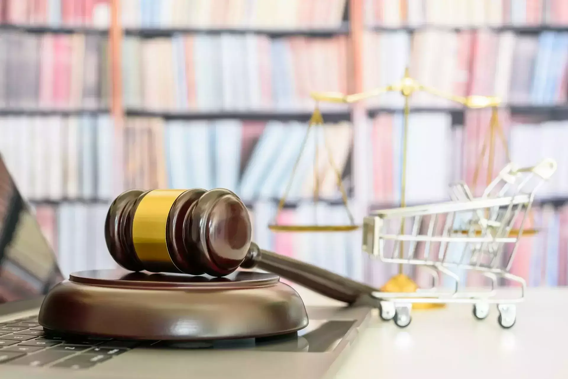 A judge's gavel and a small shopping cart on a desk with a laptop.