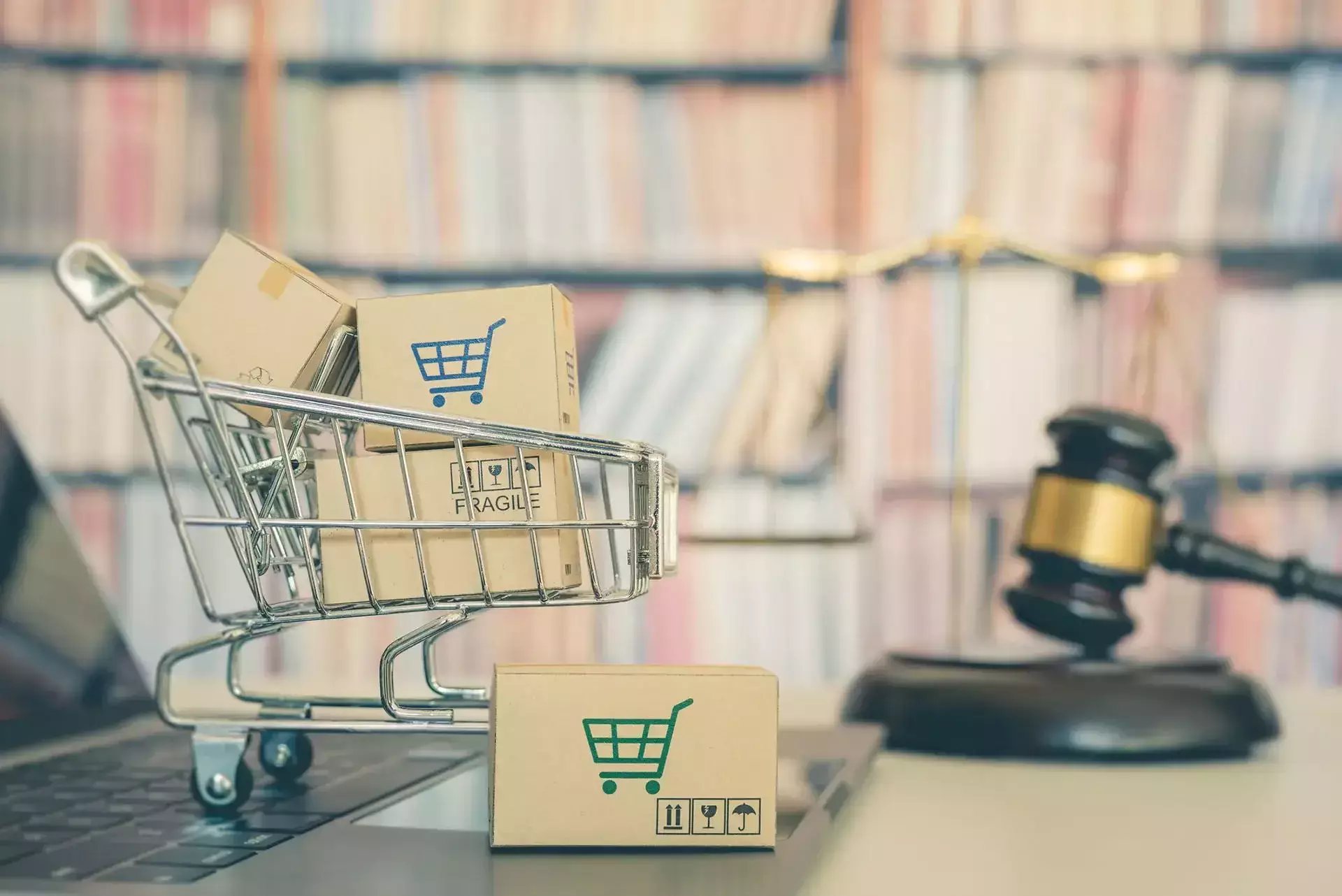 A shopping cart with boxes on a laptop next to a gavel and scales of justice.