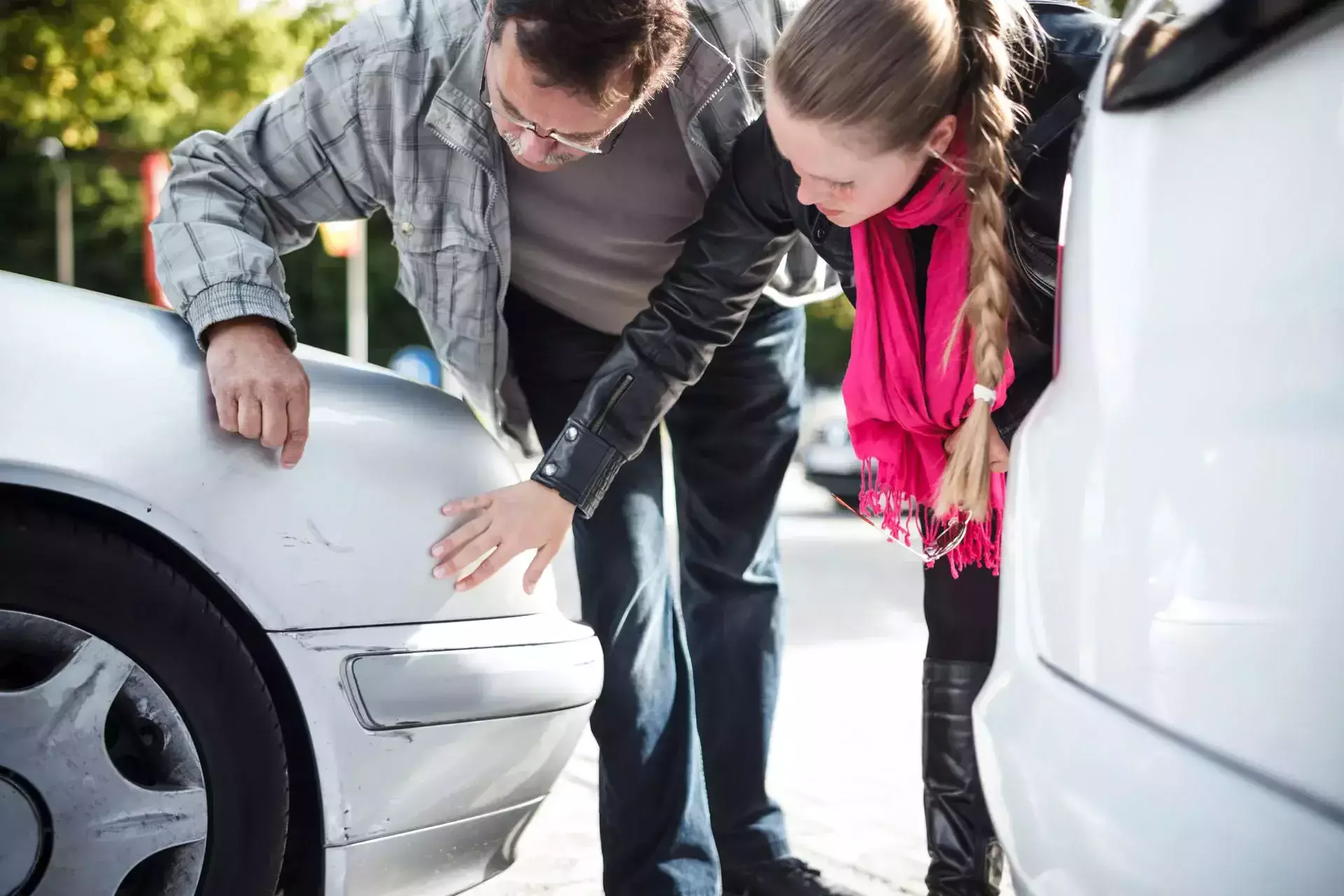 A man and woman inspecting scratches on a silver car bumper.