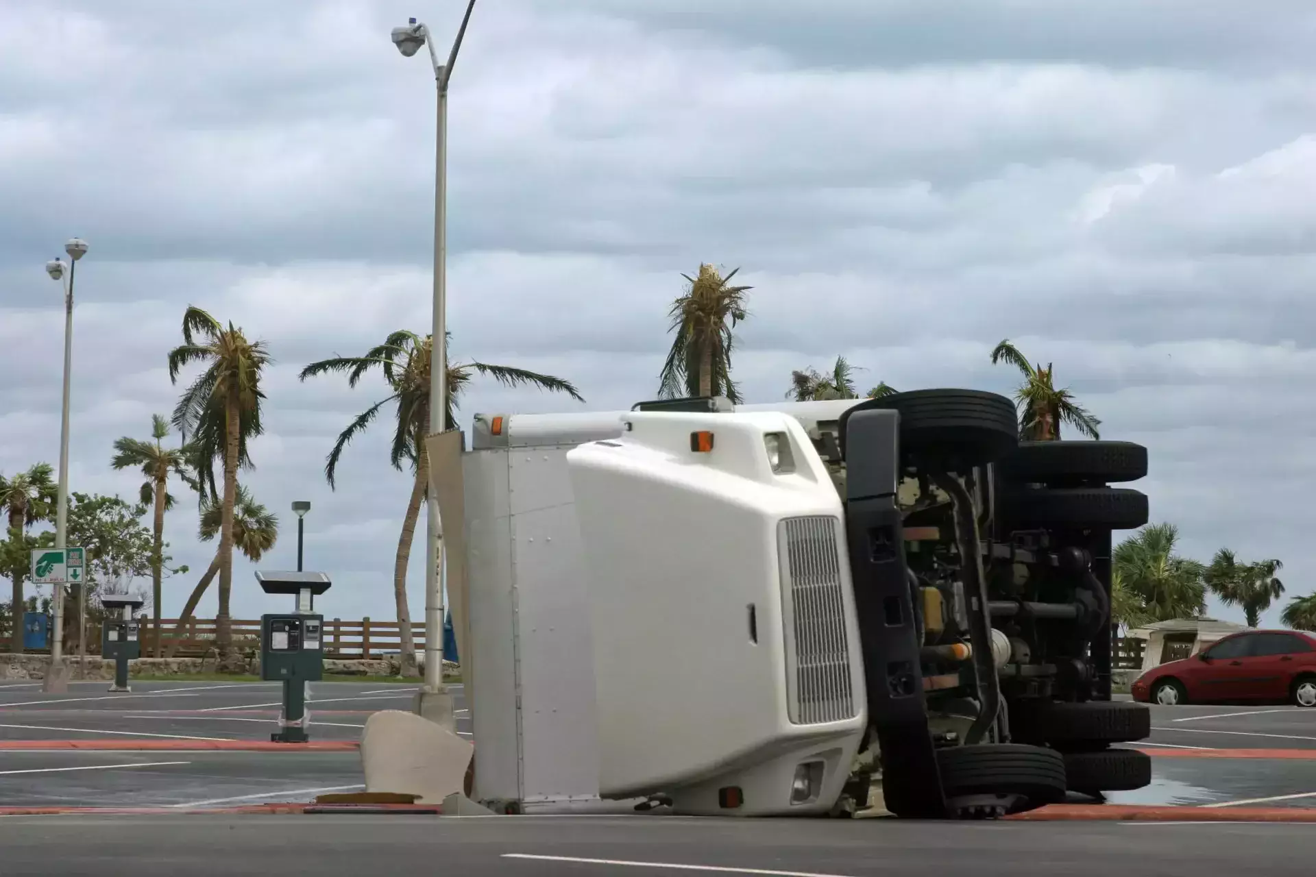 Un camión comercial grande volcó de costado cerca de una zona de estacionamiento con palmeras.