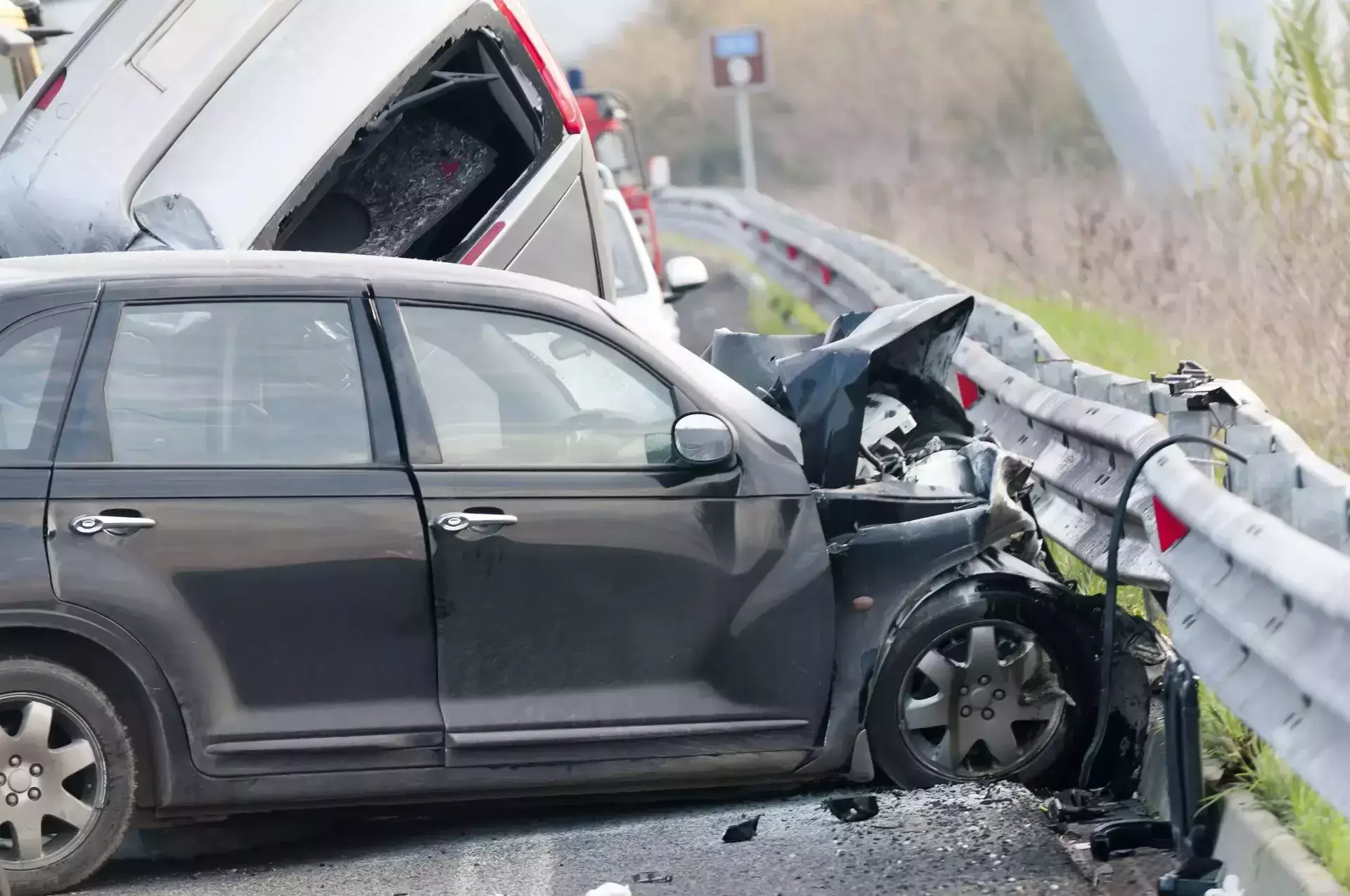 Severely damaged dark car crashed into a guardrail on a road.