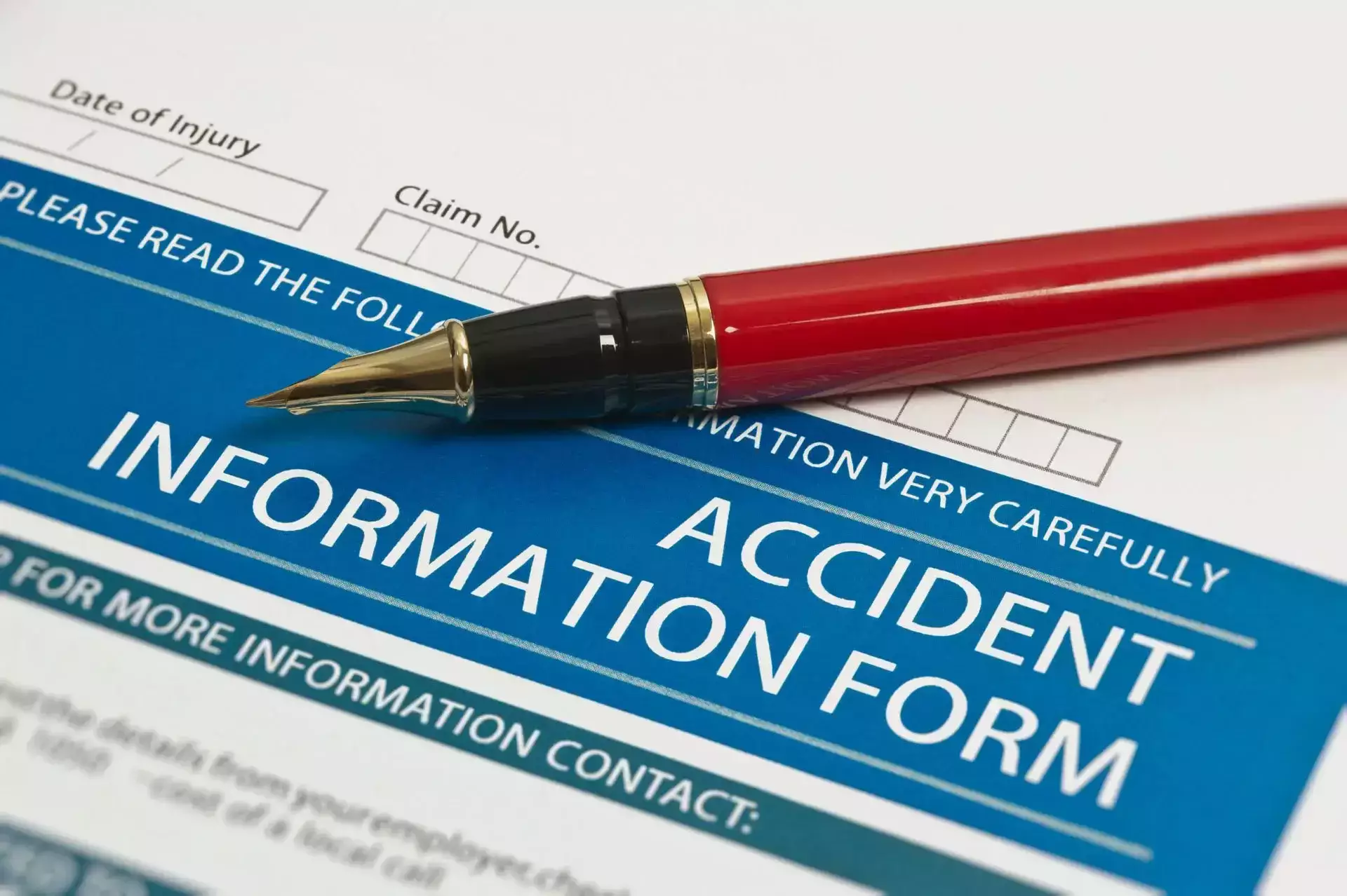 Red fountain pen resting on a blue and white accident information form with fields for date of injury and claim number.