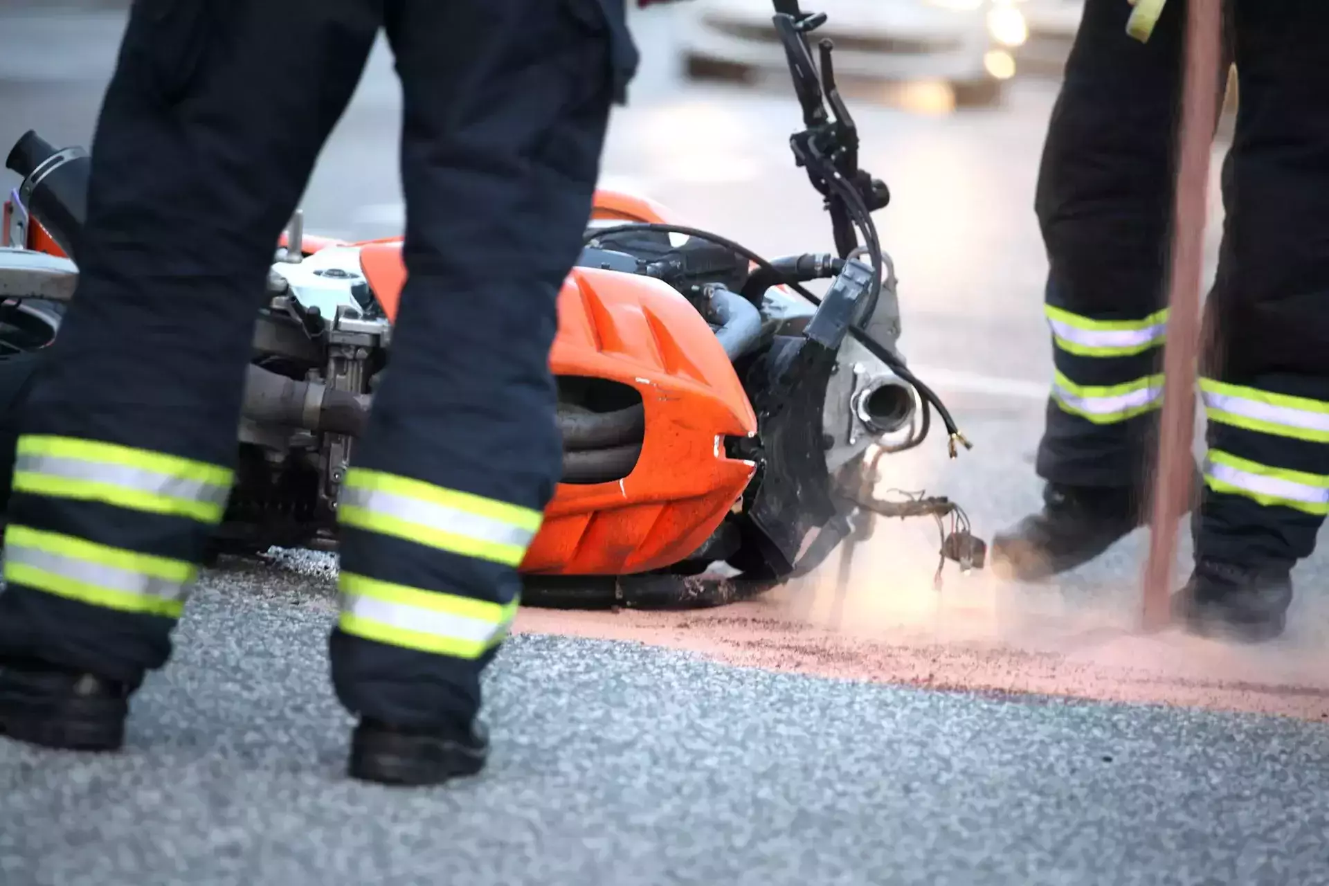 Firefighters near a crashed orange motorcycle on the pavement.