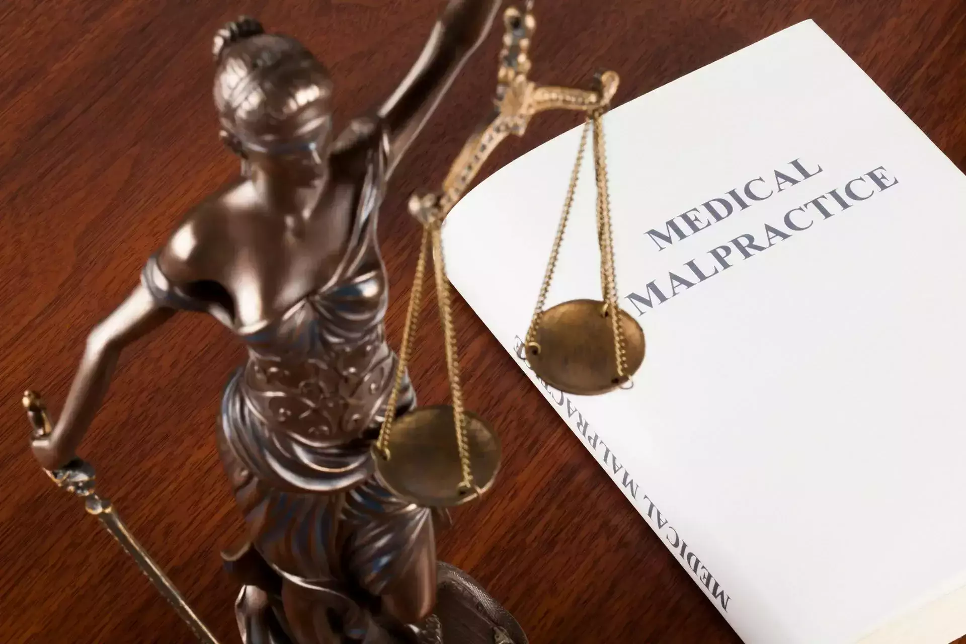 Lady Justice statue next to a book titled 'Medical Malpractice'.