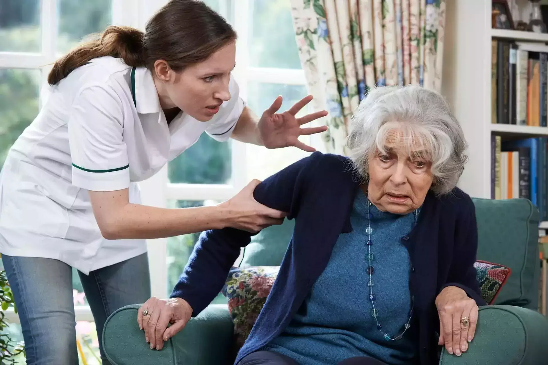 Una cuidadora agarrando del brazo a una mujer anciana en una habitación.