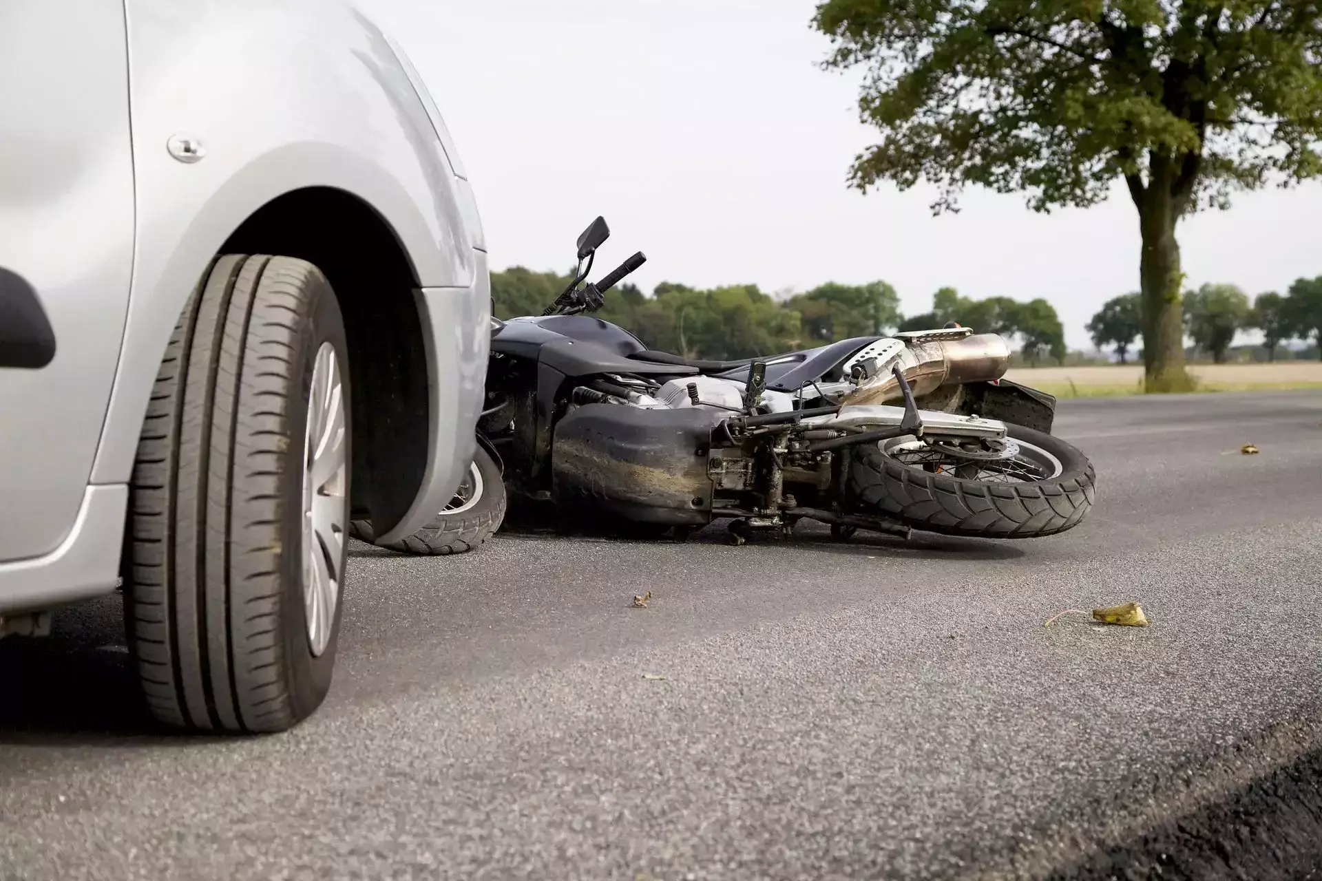 Fallen motorcycle on the road next to a silver car's tire.