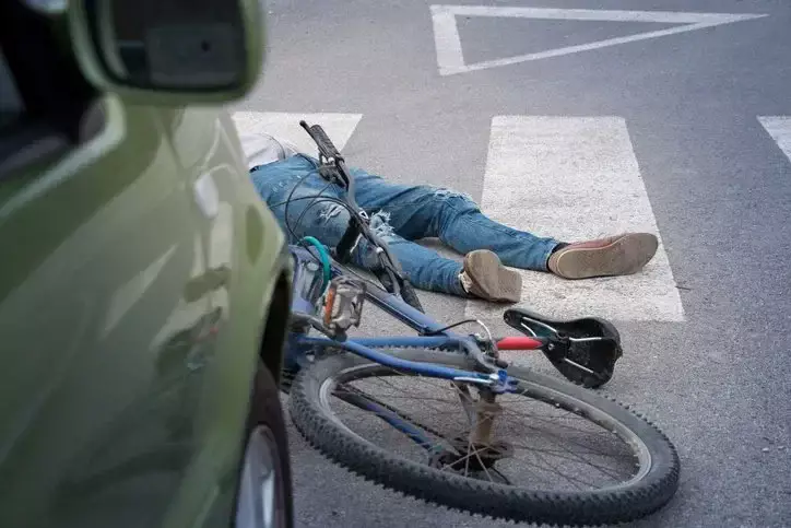Ciclista caído en la carretera junto a una bicicleta y un auto.