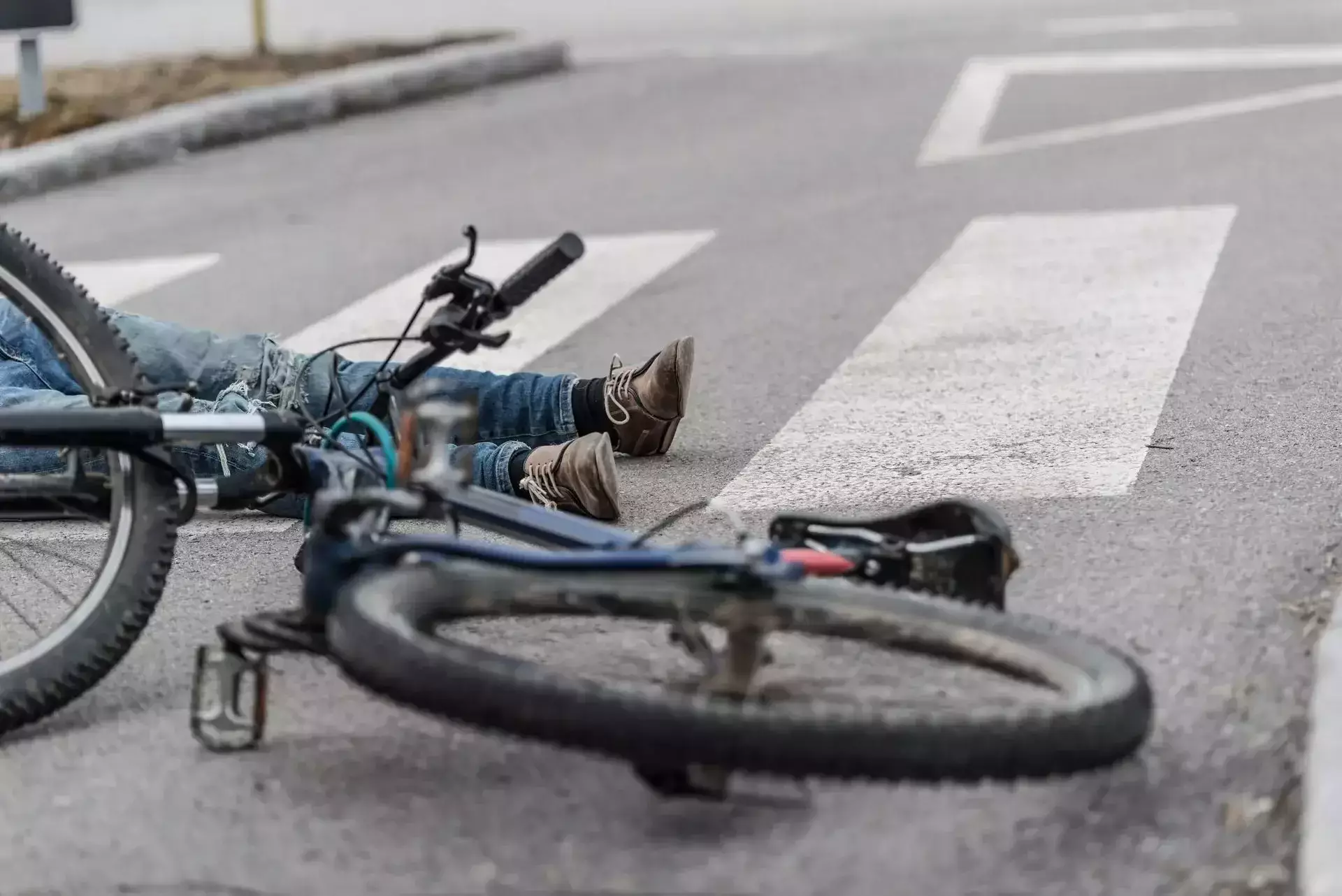 A fallen bicycle and a person on a road by a crosswalk.