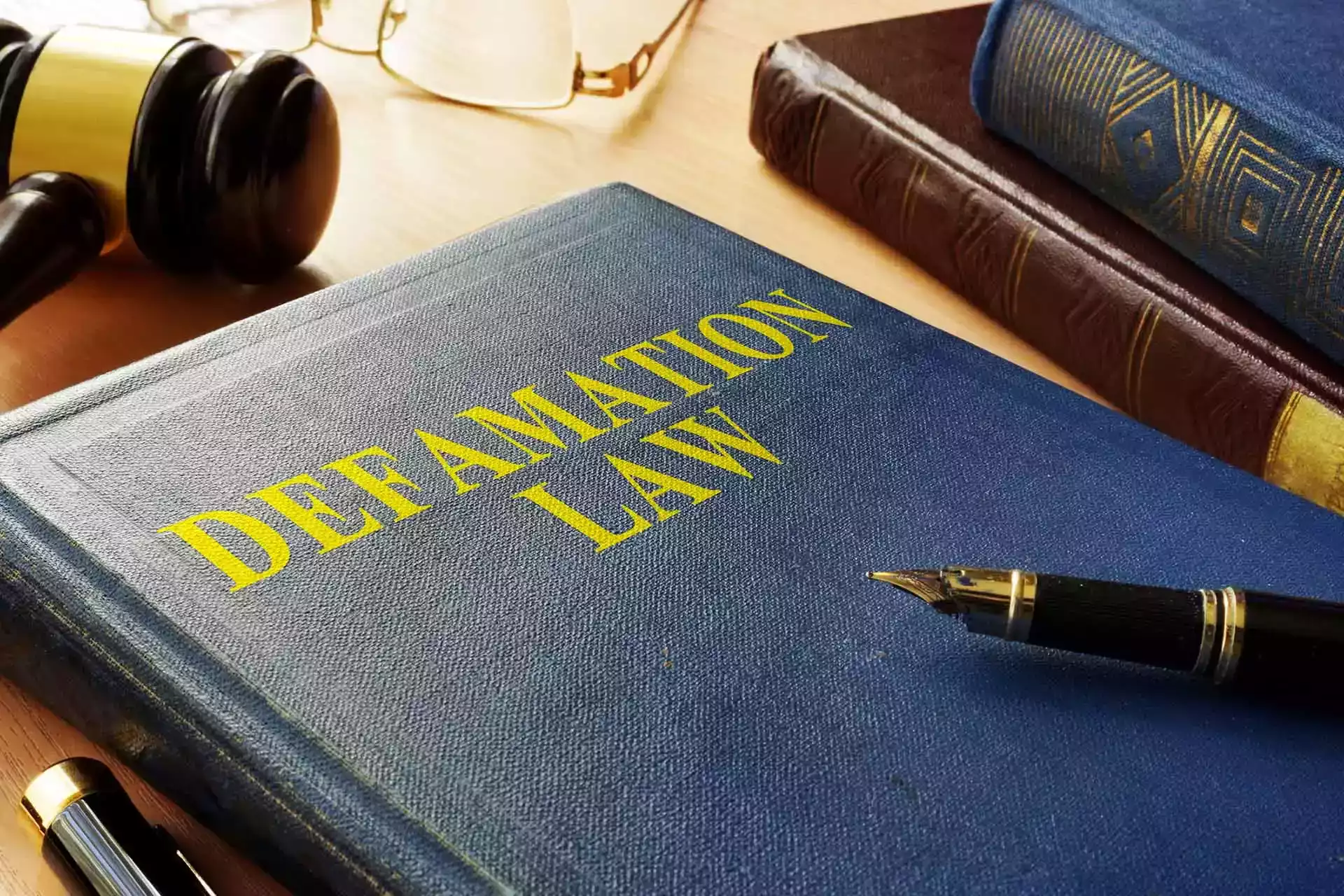 Un libro titulado 'Ley de difamación' con una pluma estilográfica y un mazo.