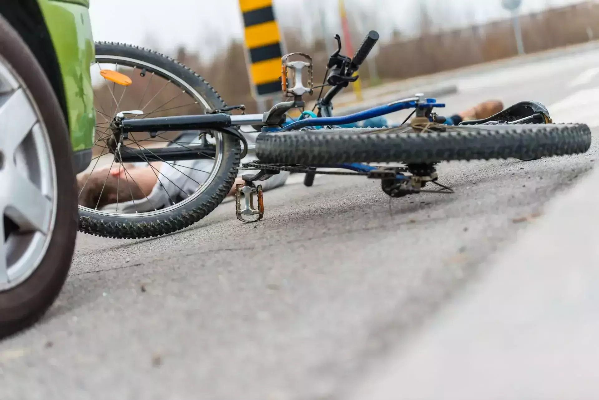 Una bicicleta caída y una persona en la carretera junto a un auto verde.