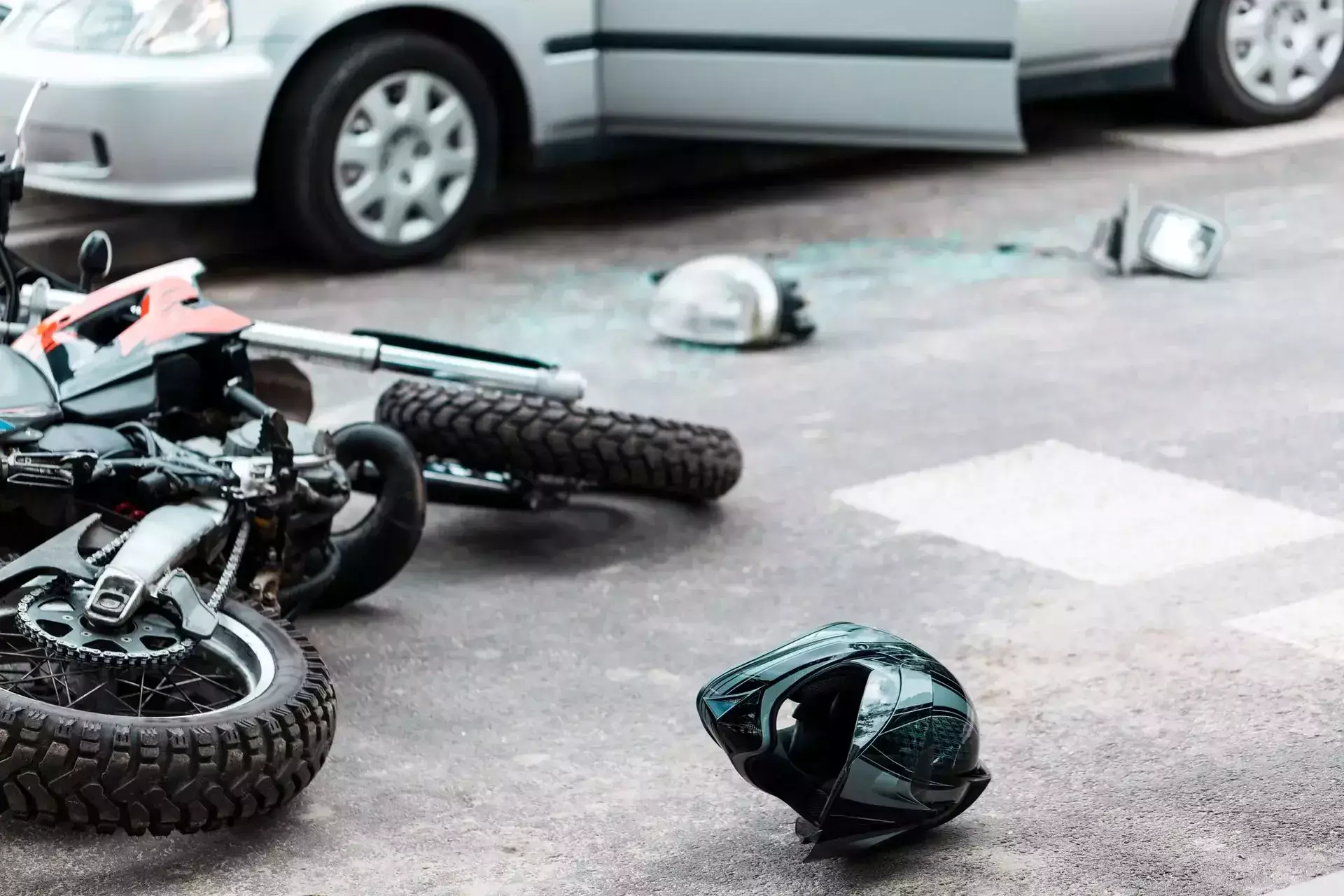 A fallen motorcycle, helmet, and debris on a road near a car.