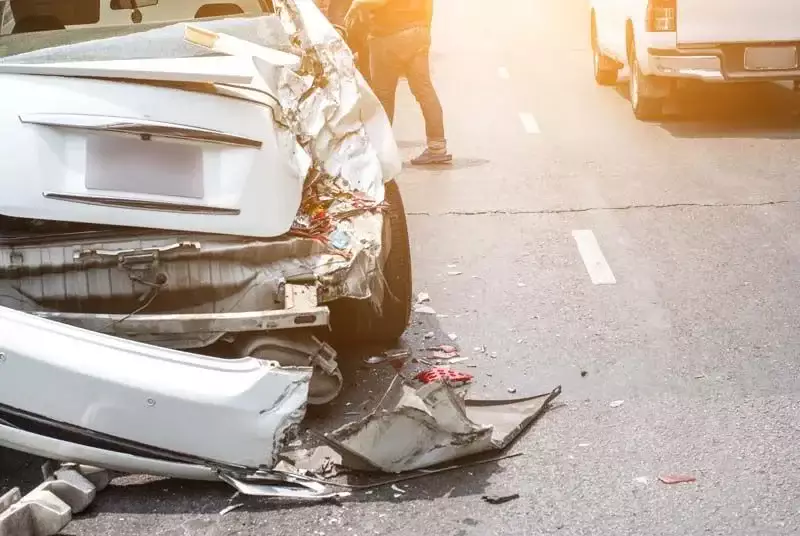 A severely damaged white car after an accident on a road.