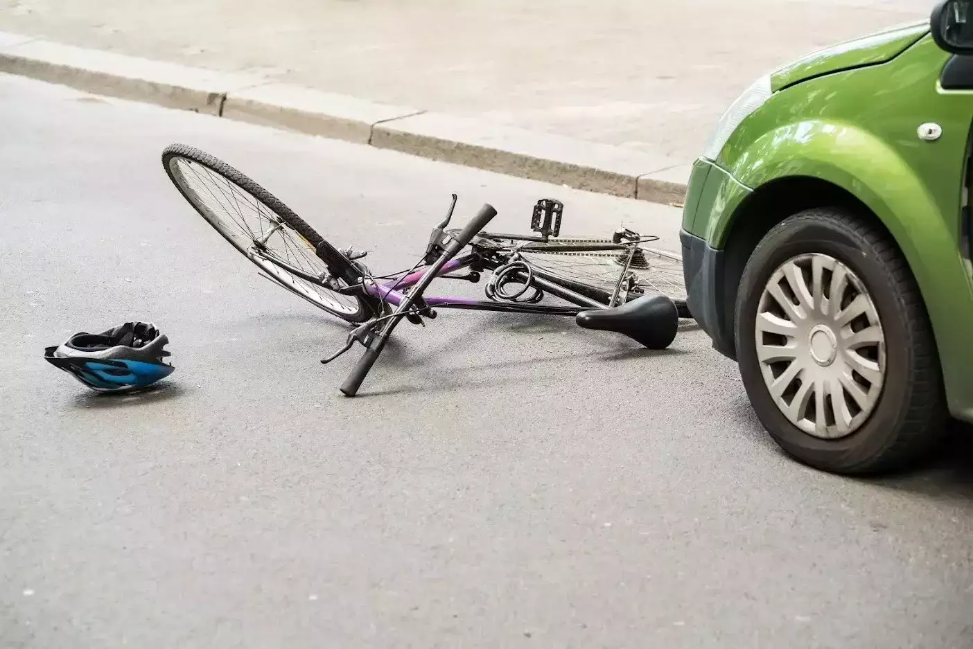 Fallen bicycle and blue helmet on the road next to a green car.