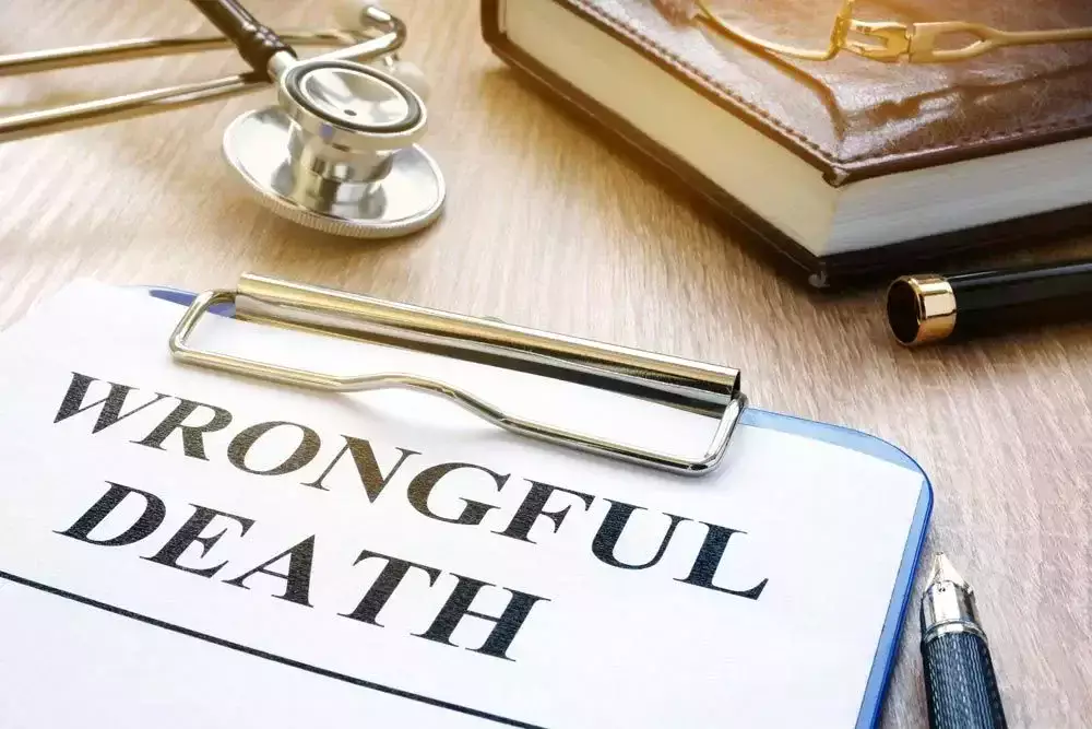 Clipboard with 'Wrongful Death' document on a desk next to a stethoscope, pen, and a closed book with glasses on top.
