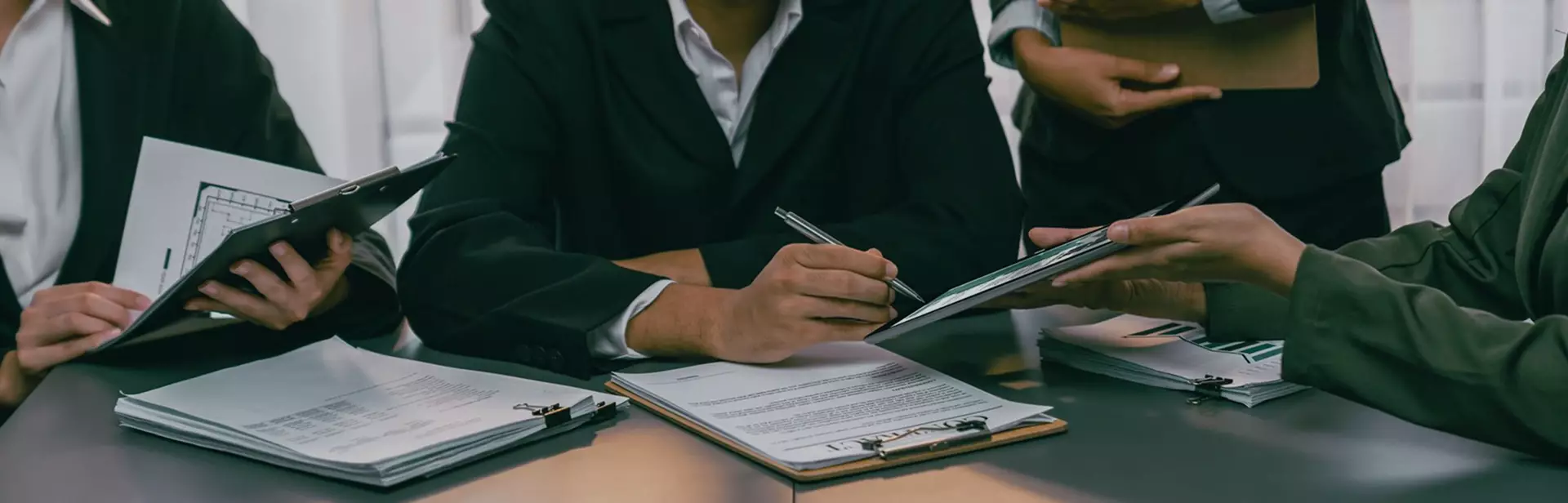 Team of professionals in suits reviewing and discussing documents and charts at a meeting table.